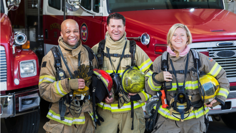 a group of 3 firefighters wearing their gear in front of a fire truck